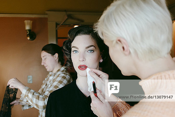 Portrait of young woman with beautician adjusting her lipstick at home