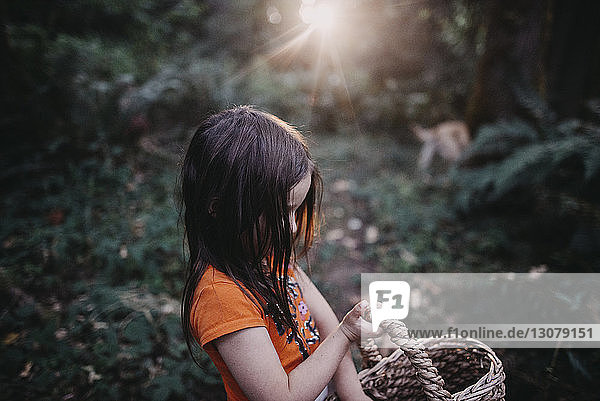 Seitenansicht eines im Wald stehenden Mädchens mit Weidenkorb