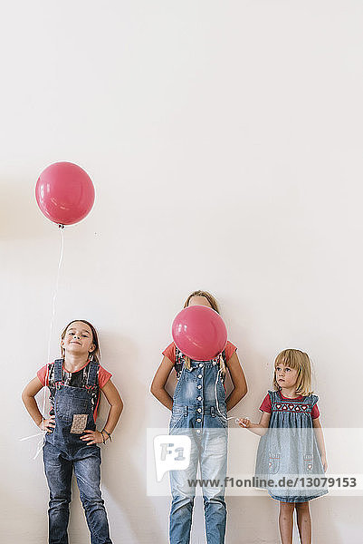 Schwestern mit Luftballons stehen zu Hause an der Wand