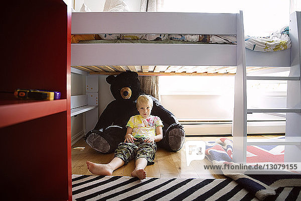 Junge in voller Länge  der zu Hause auf einem Teddybär unter dem Bett liegt
