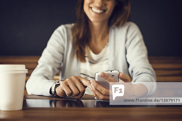 Mitschnitt einer lächelnden Frau die im Café ein Mobiltelefon benutzt