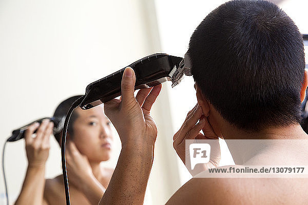 Rear view of woman shaving hair while reflecting in mirror at home