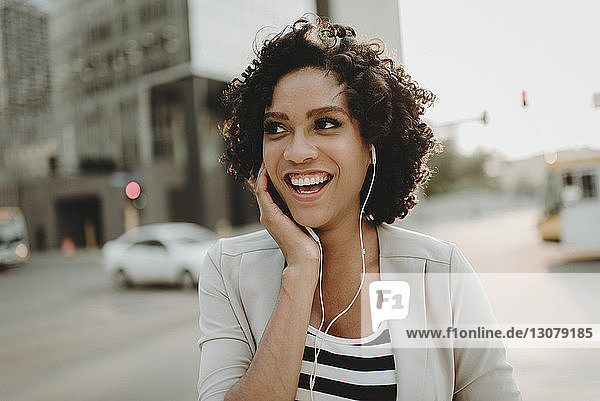 Happy woman looking away while listening music on city street
