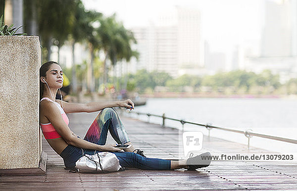 Woman listening music and relaxing on wooden walkway at park