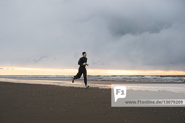Man jogging at beach against cloudy sky
