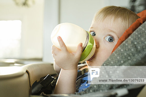 Porträt eines kleinen Jungen  der Milch trinkt  während er zu Hause auf einem Hochstuhl sitzt