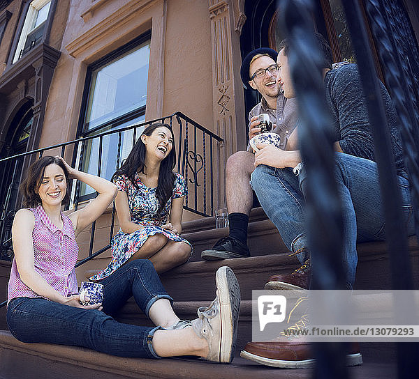 Low angle view of friends enjoying while sitting on steps outside building