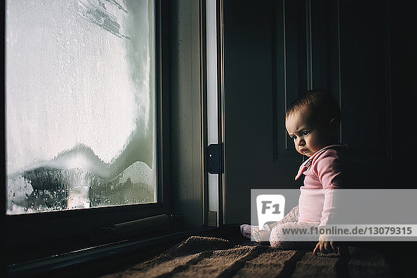 Baby girl sitting by condensed glass door at home