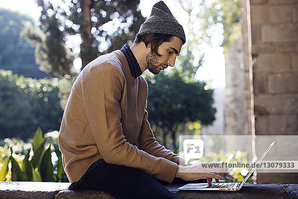 Side view of man using laptop computer retaining wall