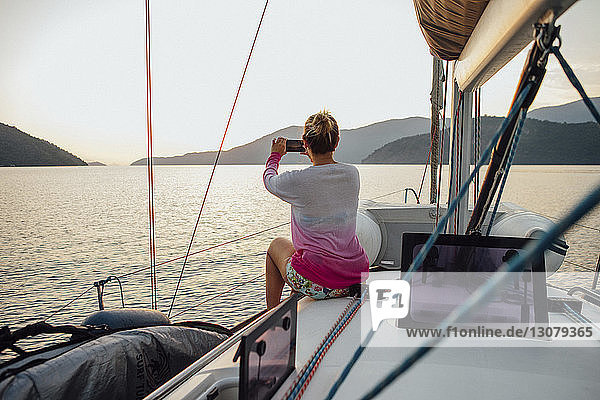 Rückansicht einer Frau  die während einer Segelbootfahrt auf See bei klarem Himmel fotografiert