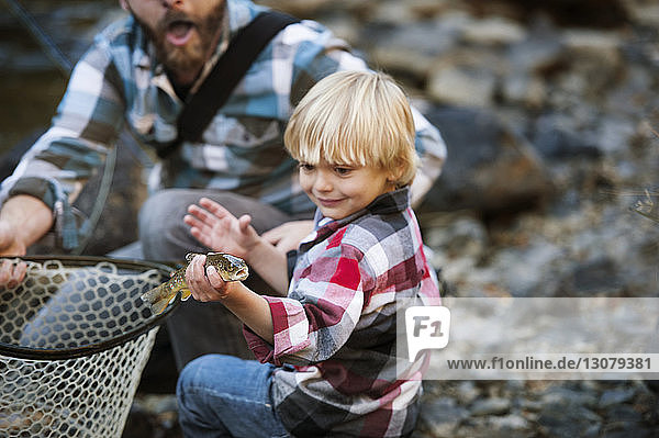 Boy holding fish while standing by father