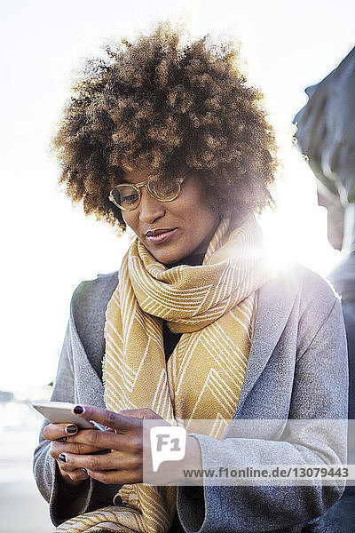 Niedriger Blickwinkel einer Frau  die ein Mobiltelefon benutzt  während sie vor klarem Himmel sitzt