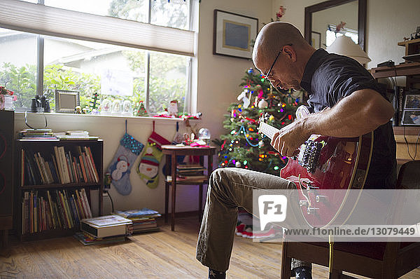 Mann spielt Gitarre  während er zu Weihnachten zu Hause auf einem Stuhl sitzt