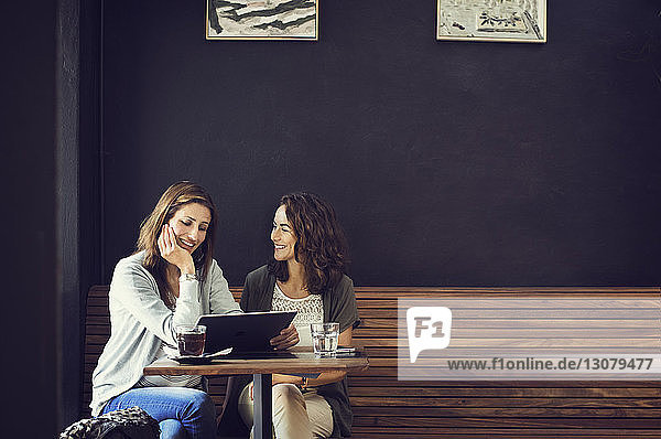 Happy female friends using tablet computer in coffee shop