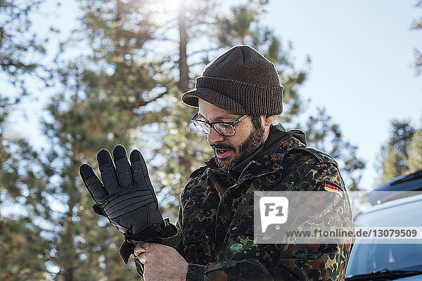 Man wearing gloves while standing against sky in forest
