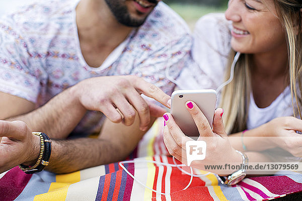Glückliches Paar benutzt Smartphone  während es am Strand auf einer Decke liegt