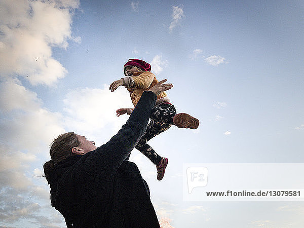 Low angle view of happy mother throwing daughter against sky