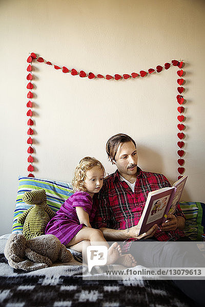 Vater liest Buch  während er mit der Tochter zu Hause im Bett sitzt