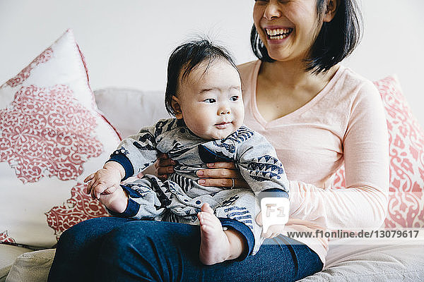 Midsection of happy mother holding cute son while sitting on sofa at home