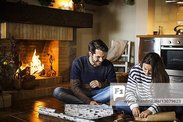 Happy couple wrapping gift boxes on floor by fireplace at home