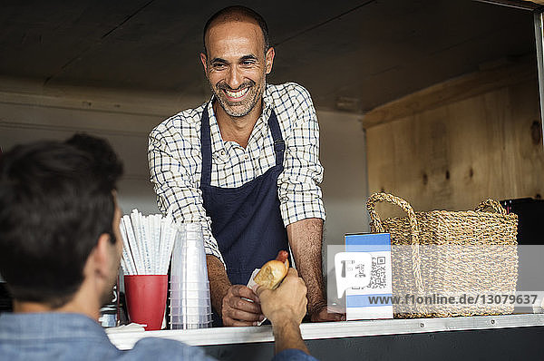Smiling male vendor giving hotdog to customer at food truck