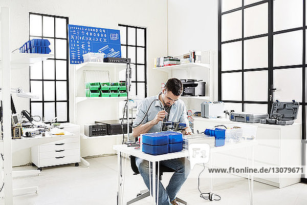 Ingenieur mit Bohrmaschine auf Leiterplatte am Tisch im Elektroniklabor