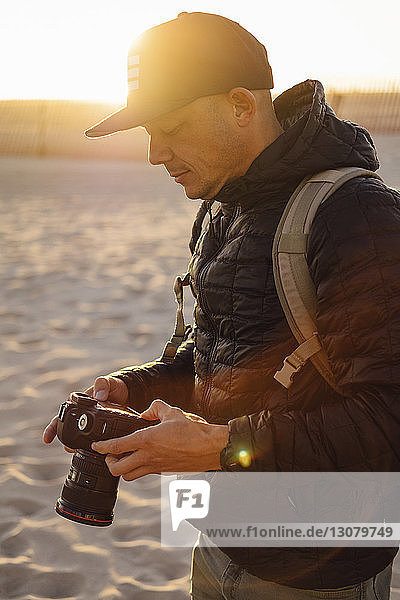 Mann mit Kamera steht bei Sonnenuntergang am Strand vor klarem Himmel