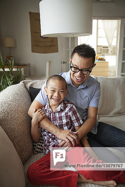 Happy father and son sitting on sofa at home