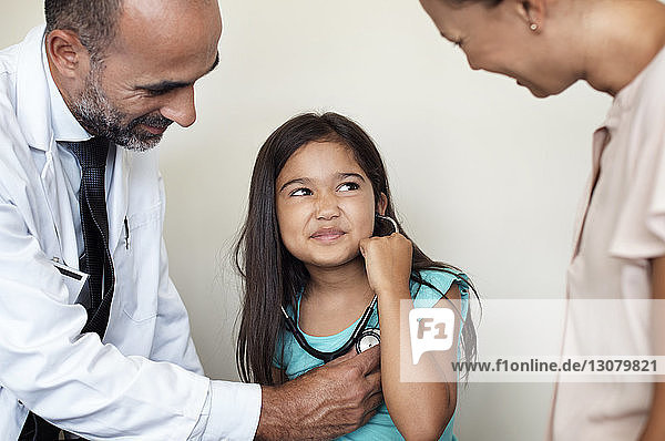 Mother and doctor looking at girl listening heartbeats in medical examination room