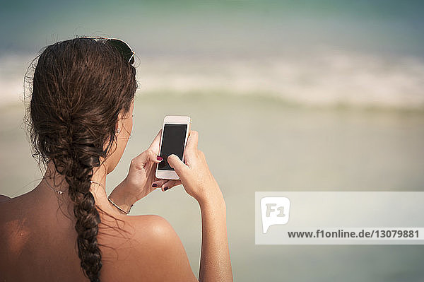 Rückansicht einer Frau mit geflochtenem Haar beim Telefonieren am Strand