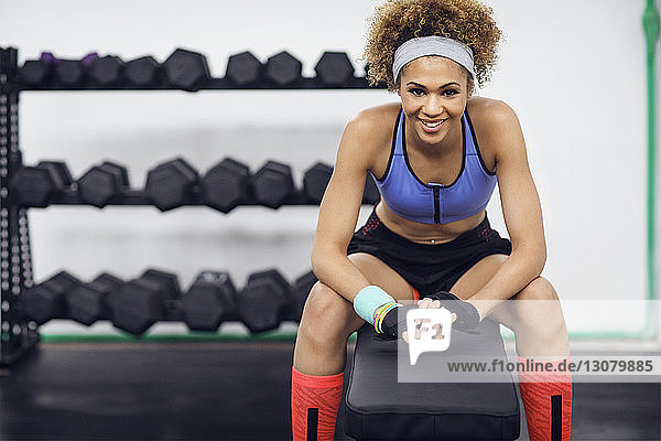 Porträt einer glücklichen Sportlerin  die in der Turnhalle auf einer Bank sitzt