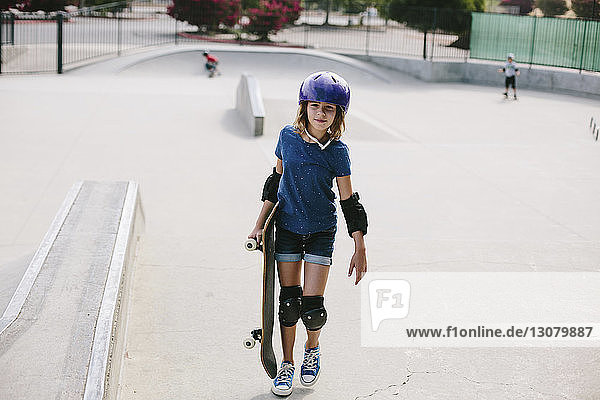 Mädchen trägt Skateboard in voller Länge beim Gehen im Park