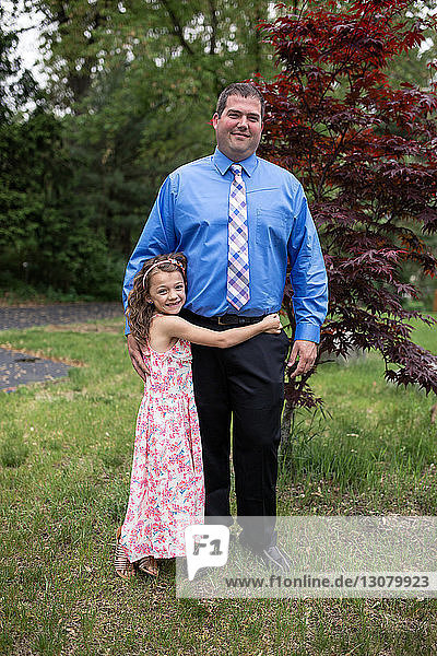 Portrait of happy daughter embracing father while standing on grassy field at park