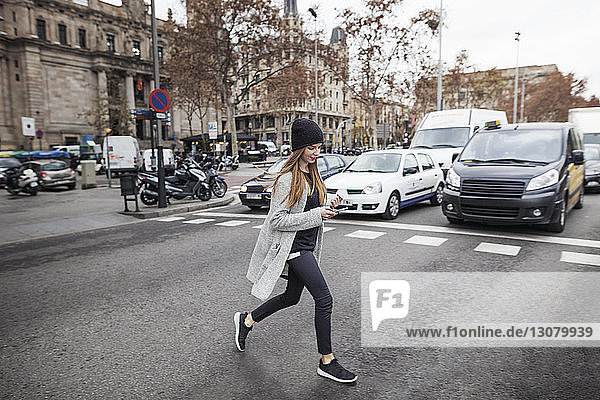 Young woman using phone while crossing city street