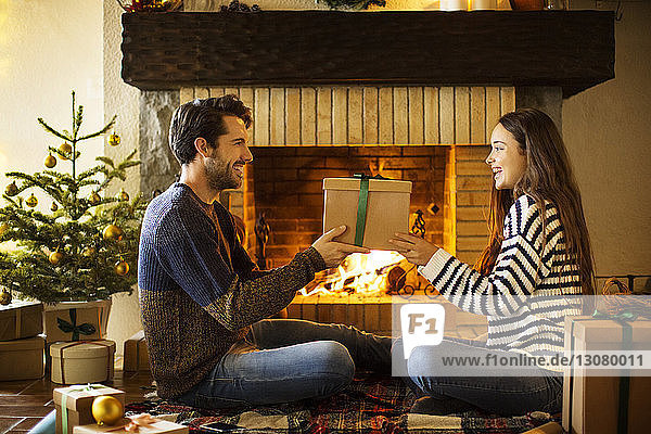 Glückliches Paar hält Weihnachtsgeschenk am Kamin zu Hause