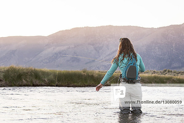 Rückansicht einer jungen Frau mit Rucksack beim Fliegenfischen im Owens River vor Bergen