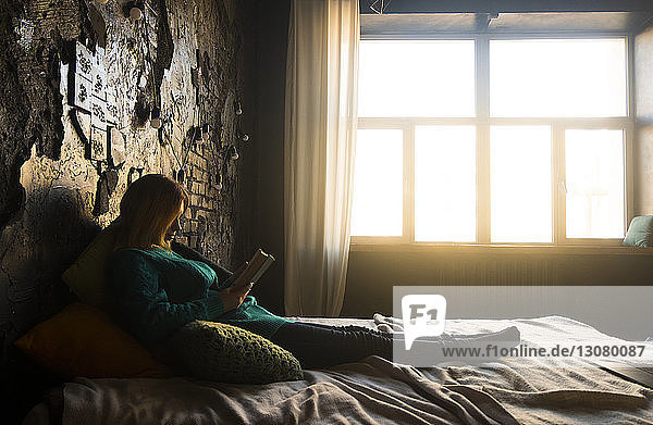 Teenage girl reading book while lying on bed at home