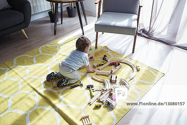 Hochwinkelaufnahme eines kleinen Jungen  der zu Hause mit einer Spielzeugeisenbahn spielt