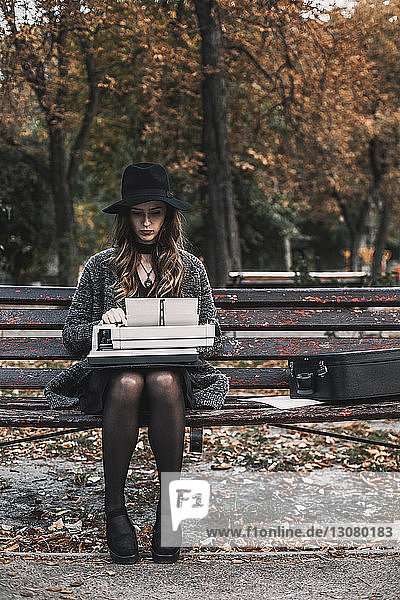 Schriftstellerin benutzt Schreibmaschine  während sie im Herbst auf einer Parkbank sitzt