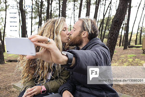 Romantisches Pärchen  das sich küsst  während es sich durch ein Smartphone im Wald durchsetzt