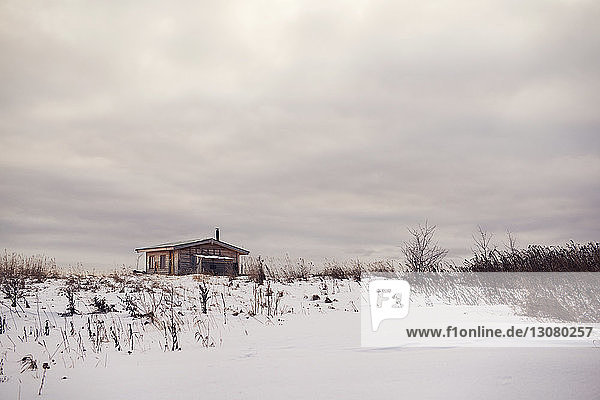 Haus auf schneebedecktem Feld vor bewölktem Himmel
