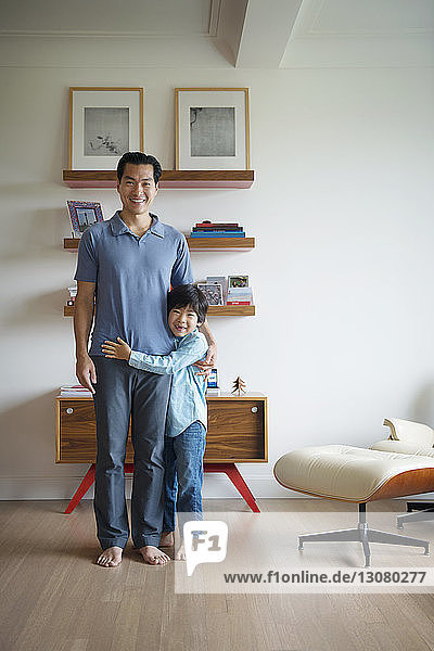 Portrait of happy father and son standing against wall at home