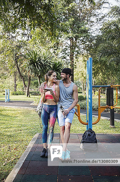 Front view of happy couple leaning over exercise equipment at park