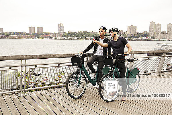 Freunde fahren Fahrrad auf der Promenade durch die Stadt gegen den klaren Himmel