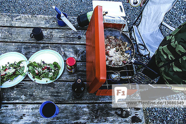 Schrägaufnahme eines Mannes  der auf dem Grill auf dem Campingplatz Essen zubereitet