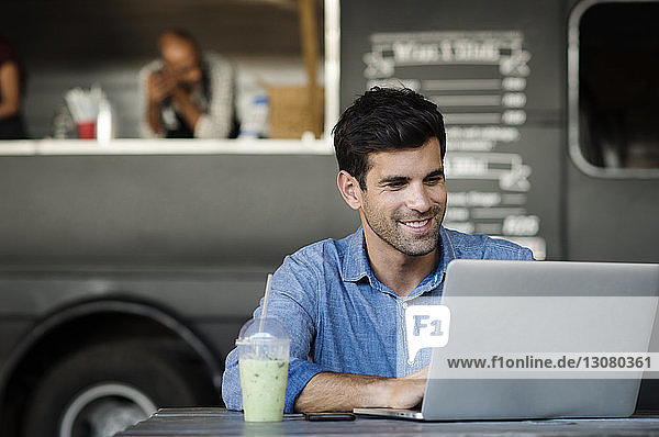 Mann benutzt Laptop-Computer  während er am Tisch auf der Straße gegen Verkäufer im Speisewagen sitzt