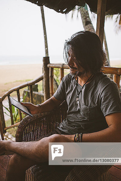 Mann benutzt Tablet-Computer  während er am Strand sitzt