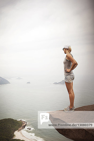 Frau steht auf Klippe und schaut auf das Meer im Nebel