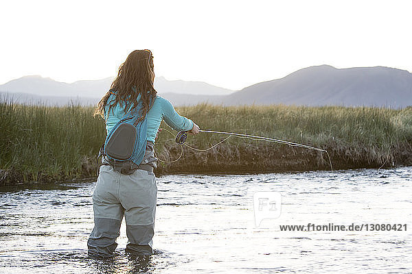 Rückansicht einer jungen Frau beim Fliegenfischen im Owens River gegen die Berge