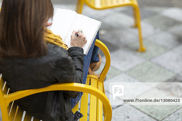 Schrägansicht einer Frau  die auf einer Bank in der Stadt sitzt und schreibt